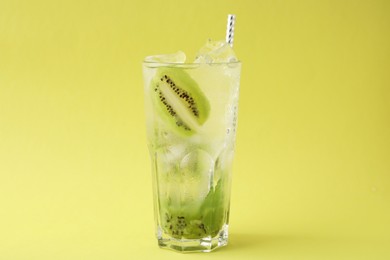 Glass of refreshing drink with kiwi on yellow background