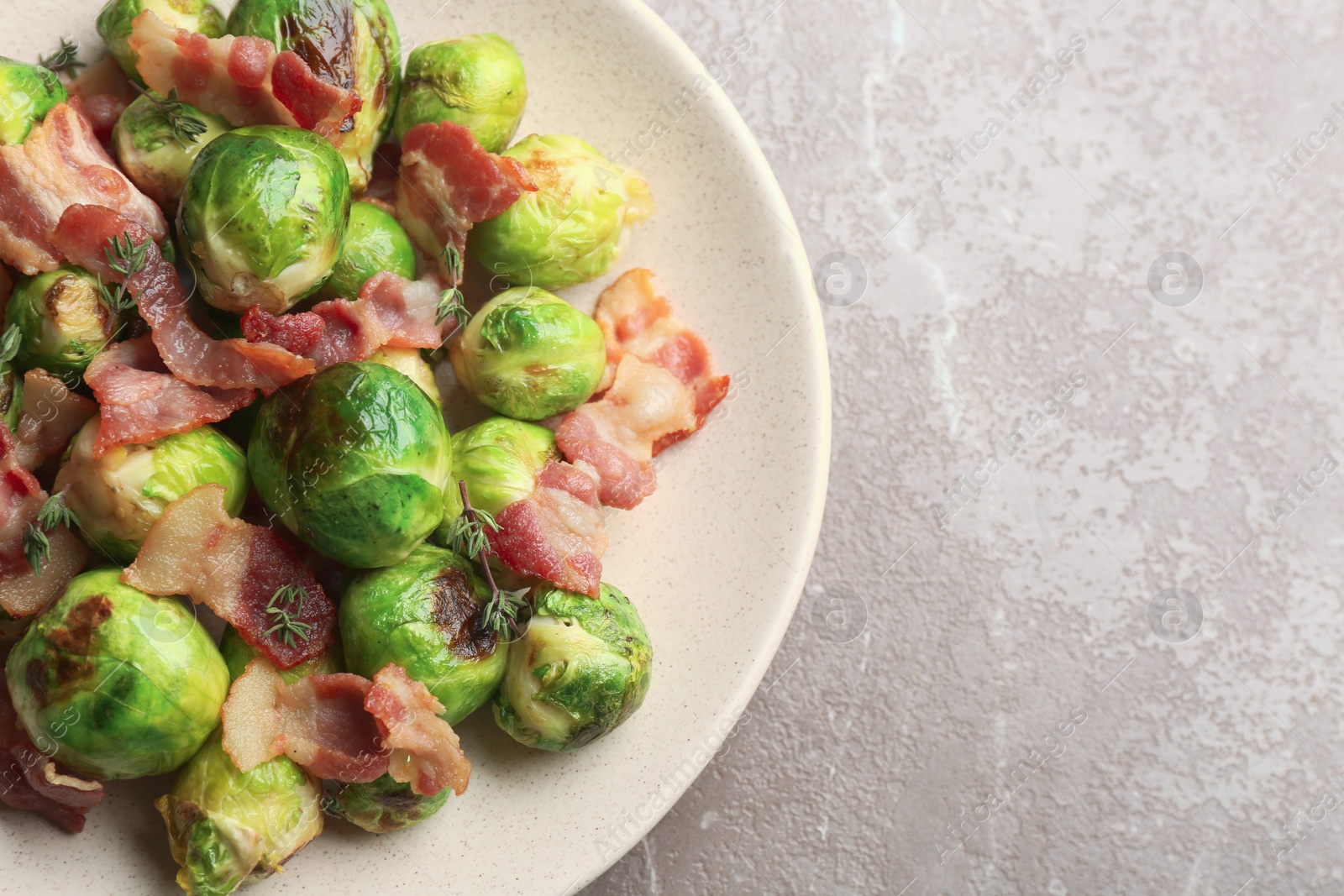 Photo of Delicious Brussels sprouts with bacon on marble table, top view. Space for text