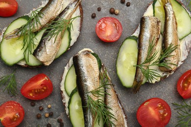 Photo of Delicious sandwiches with sprats, cucumber and dill served on grey table, flat lay