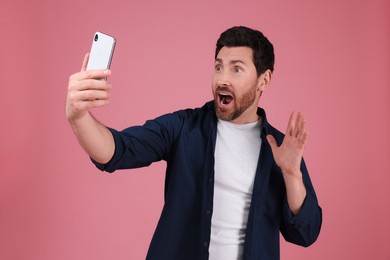 Smiling man taking selfie with smartphone on pink background