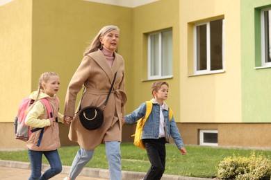 Photo of Being late for school. Senior woman and her grandchildren with backpacks running outdoors