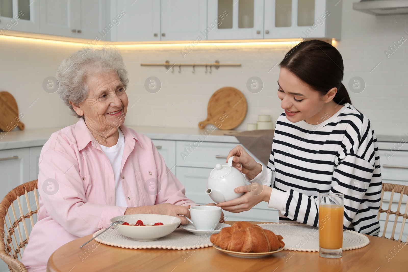 Photo of Young caregiver serving breakfast for senior woman at table in kitchen. Home care service