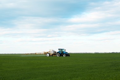 Photo of Tractor spraying pesticide in field on spring day. Agricultural industry