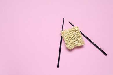 Instant noodles and chopsticks on pink background, flat lay. Space for text