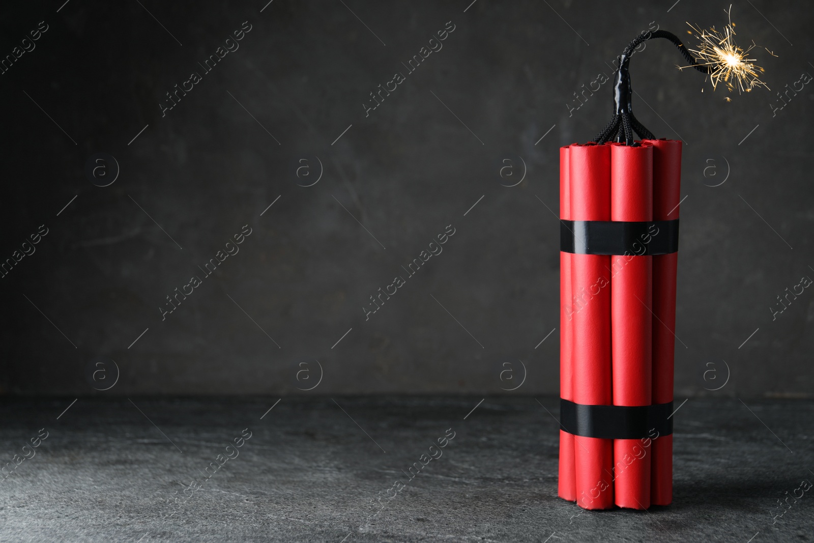 Photo of Dynamite bomb with lit fuse on grey table, space for text