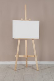 Photo of Wooden easel with blank canvas near beige wall