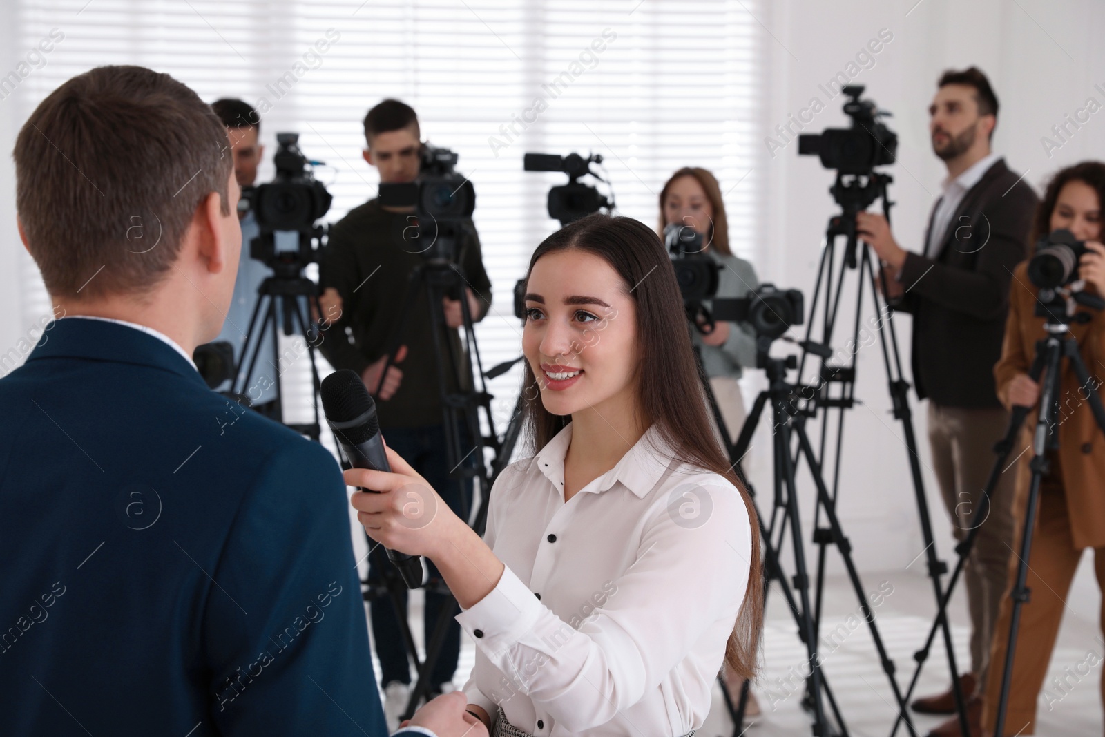 Photo of Professional young journalist interviewing businessman and group of video camera operators on background