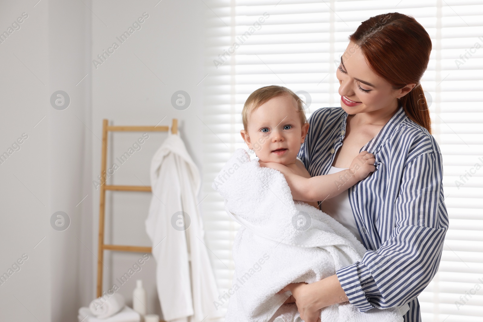 Photo of Mother holding cute little baby wrapped with towel after bath indoors. Space for text