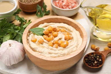 Photo of Delicious hummus with chickpeas and different ingredients on white wooden table, closeup