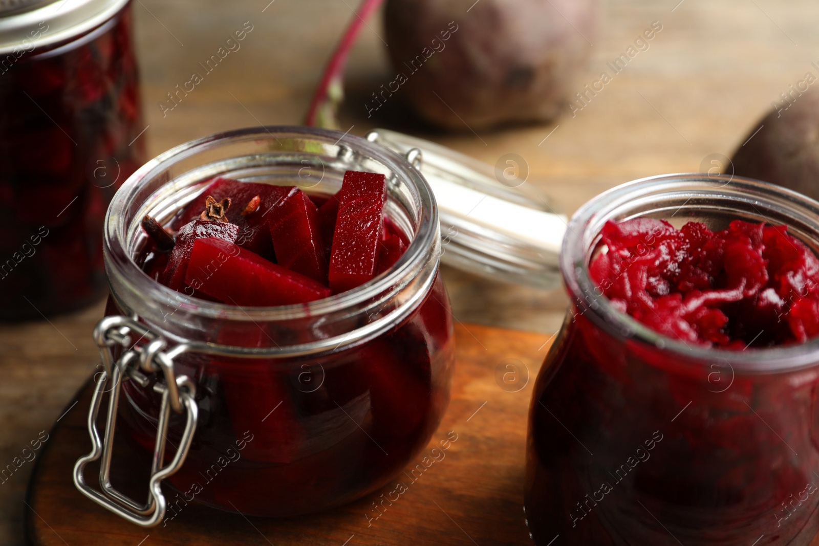 Photo of Jars with delicious pickled beets on wooden board, closeup