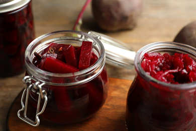 Photo of Jars with delicious pickled beets on wooden board, closeup