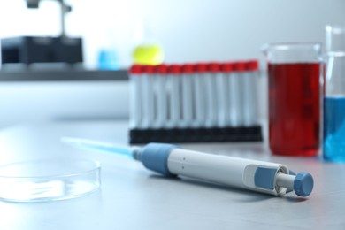 Photo of Laboratory analysis. Micropipette, petri dish, beakers with liquids and test tubes on grey table, closeup