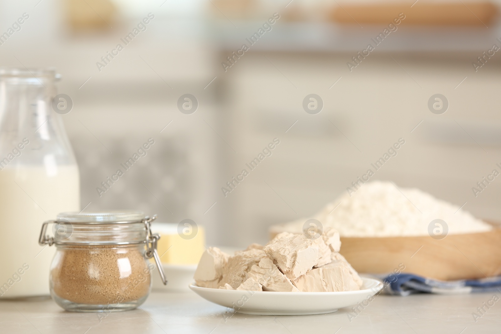 Photo of Yeast and dough ingredients on white table indoors, space for text