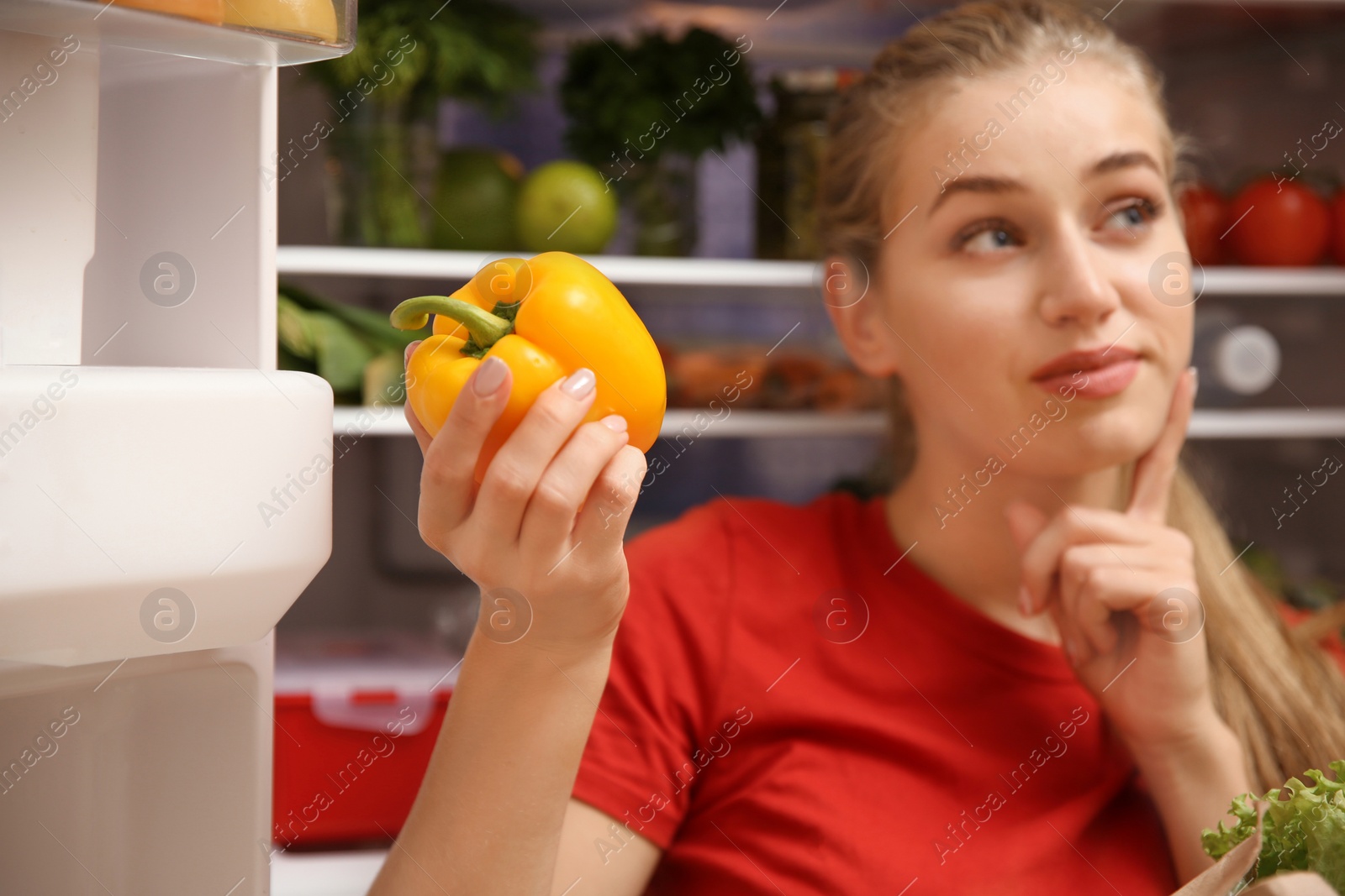 Photo of Young woman with fresh bell pepper near refrigerator at home