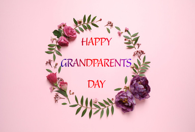 Frame made of beautiful flowers and phrase HAPPY GRANDPARENTS DAY on pink background, flat lay. Floral composition