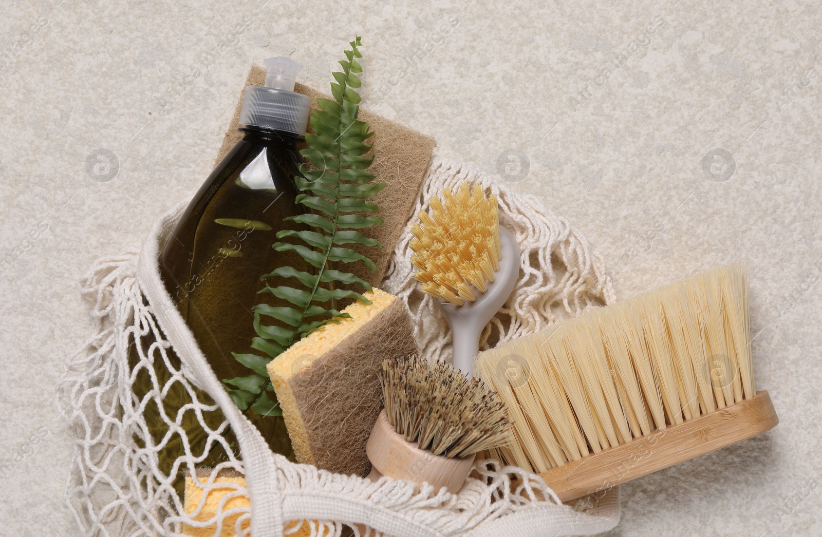 Photo of Different cleaning supplies in string bag on beige background, top view. Space for text