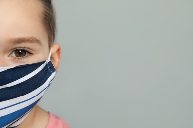 Photo of Cute little girl in protective mask on grey background, closeup. Space for text