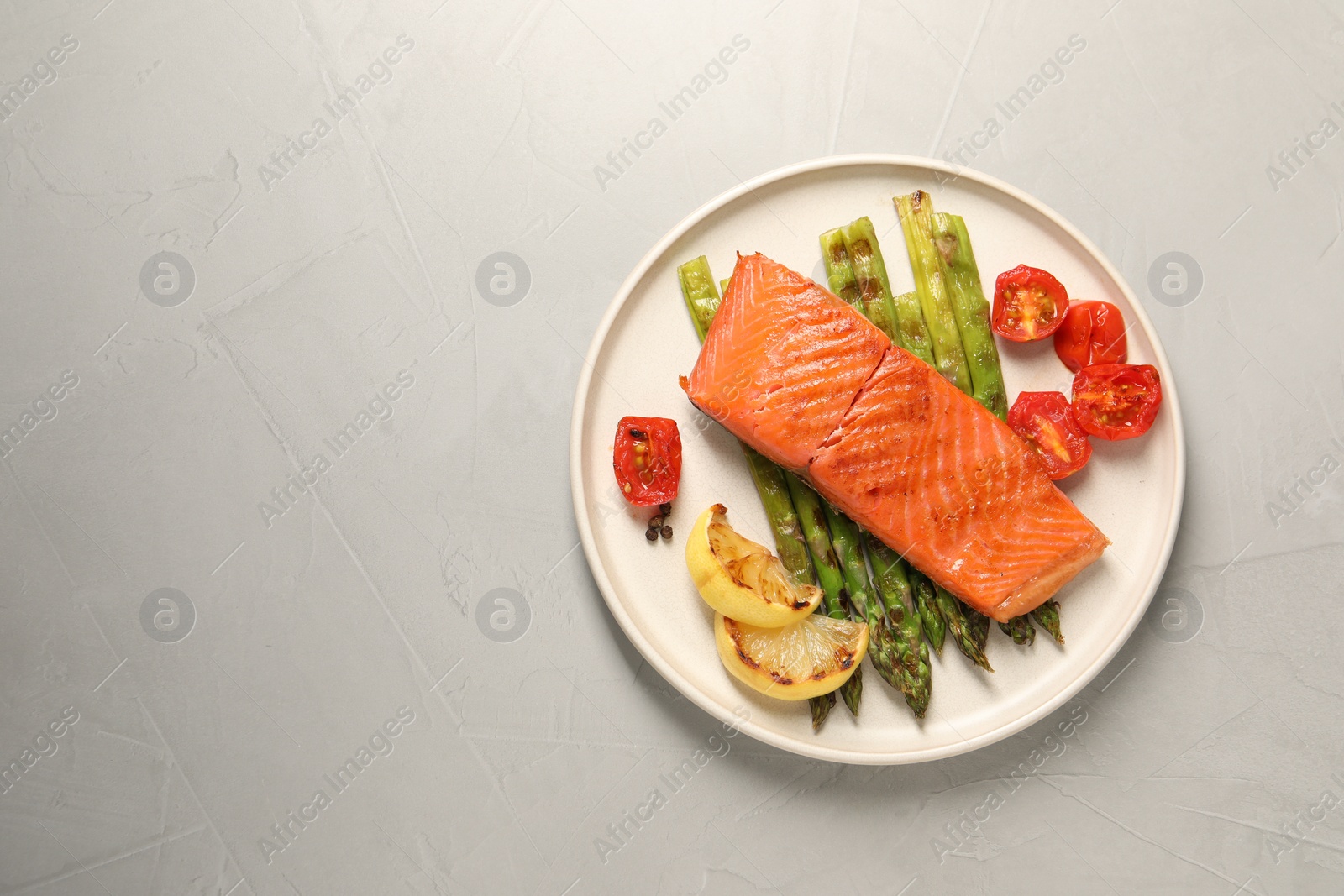 Photo of Tasty grilled salmon with asparagus, tomatoes, spices and lemon on light grey table, top view. Space for text