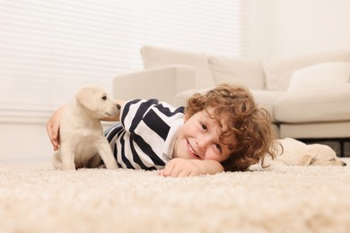 Photo of Little boy with cute puppies on beige carpet at home