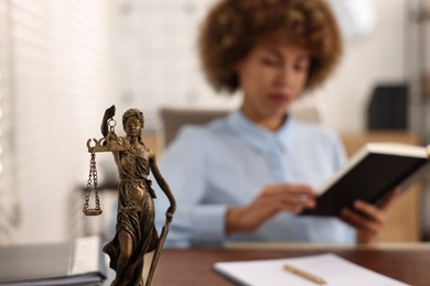 Photo of Notary with notebook at workplace in office, focus on statue of Lady Justice