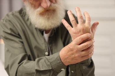 Senior man suffering from pain in hand on blurred background, closeup. Rheumatism symptom