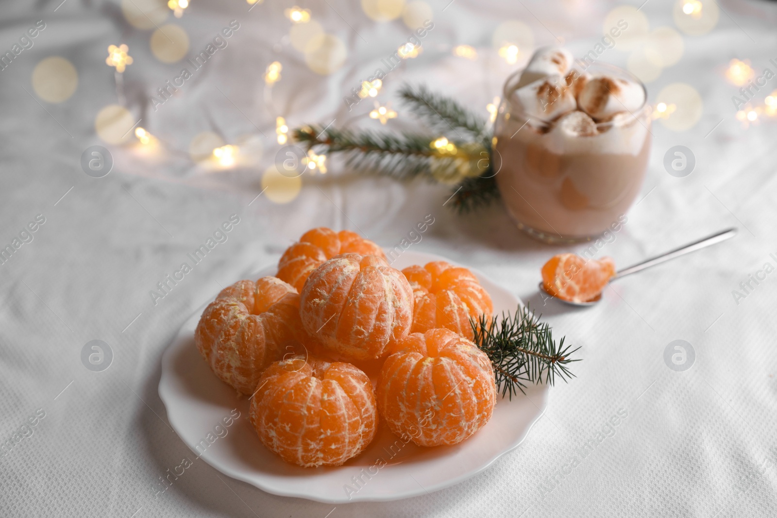 Photo of Peeled delicious ripe tangerines and glass of drink with marshmallows on white bedsheet