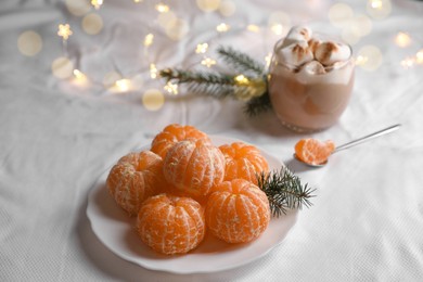 Peeled delicious ripe tangerines and glass of drink with marshmallows on white bedsheet