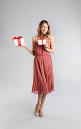 Beautiful young woman with Christmas presents on light grey background