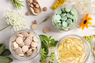 Photo of Different pills, flowers and herbs on white wooden table, flat lay. Dietary supplements