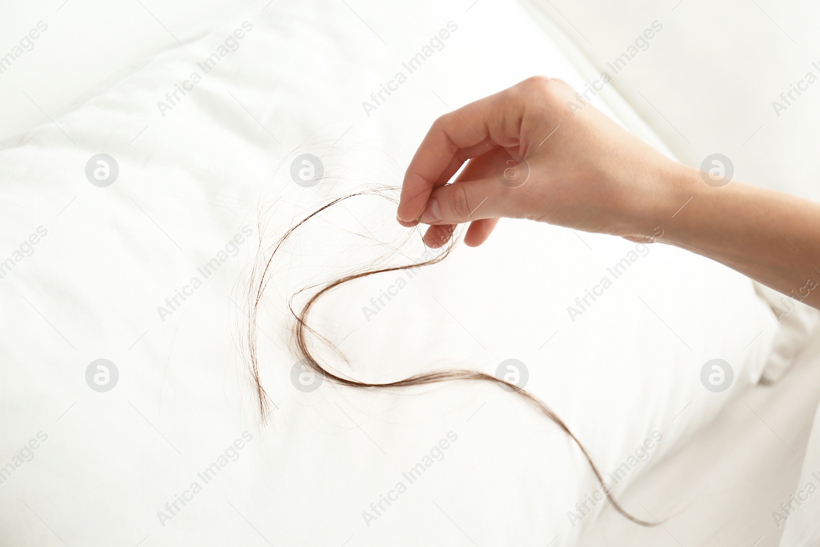 Photo of Woman picking fallen long hair from pillow, closeup