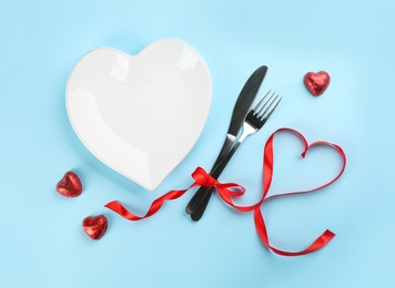 Beautiful table setting for Valentine's Day dinner on light blue background, flat lay