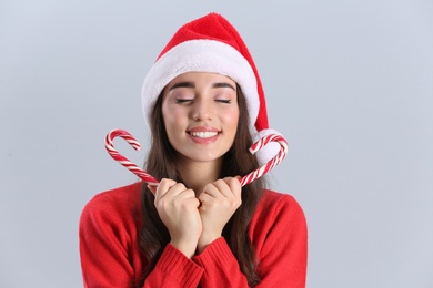 Beautiful woman in Santa Claus hat holding candy canes on light grey background