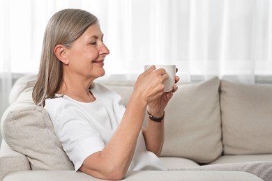 Photo of Senior woman with cup of tea on sofa at home