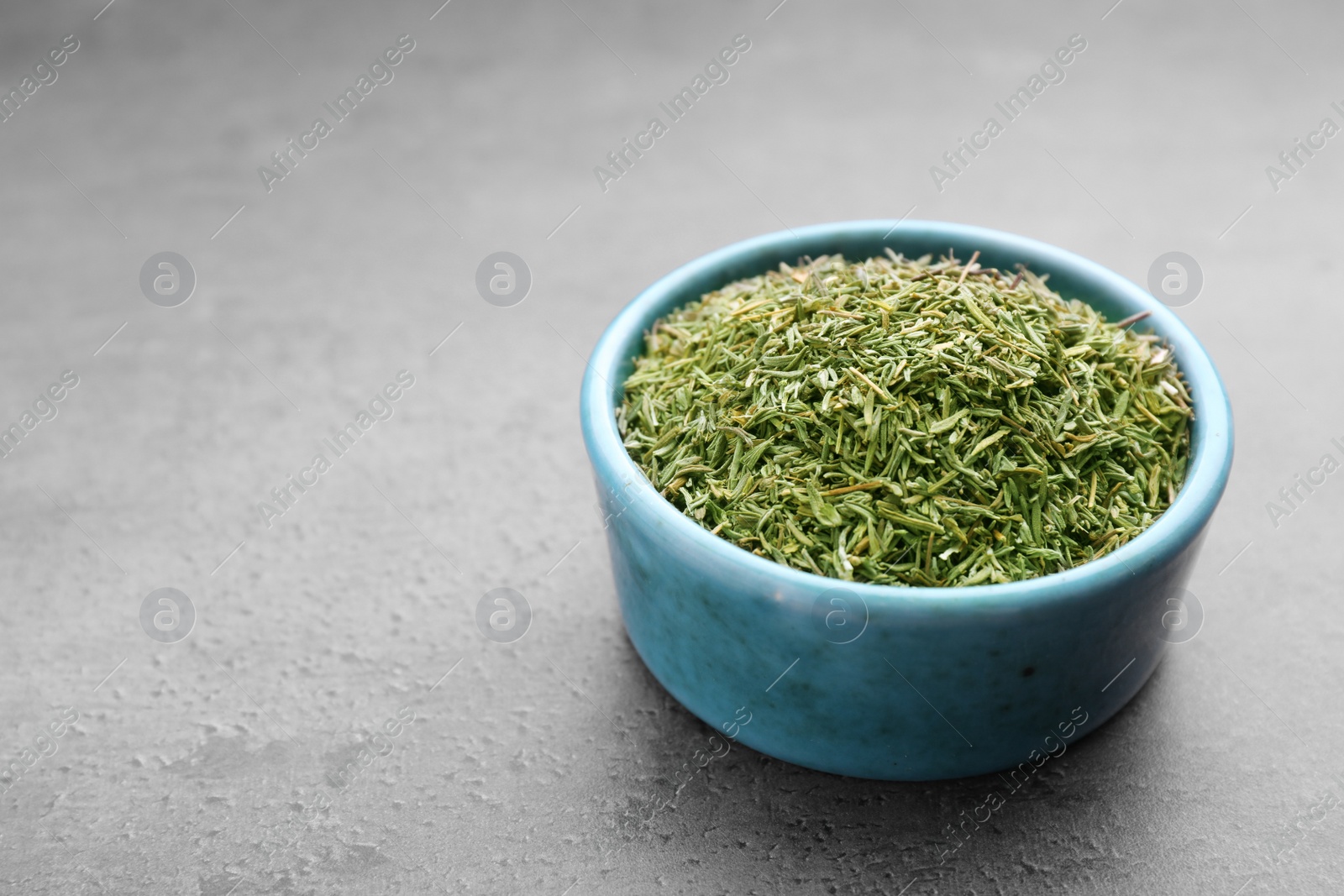 Photo of Bowl with dried thyme on grey table, closeup. Space for text
