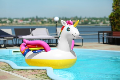 Photo of Funny inflatable unicorn ring floating in swimming pool on sunny day, outdoors