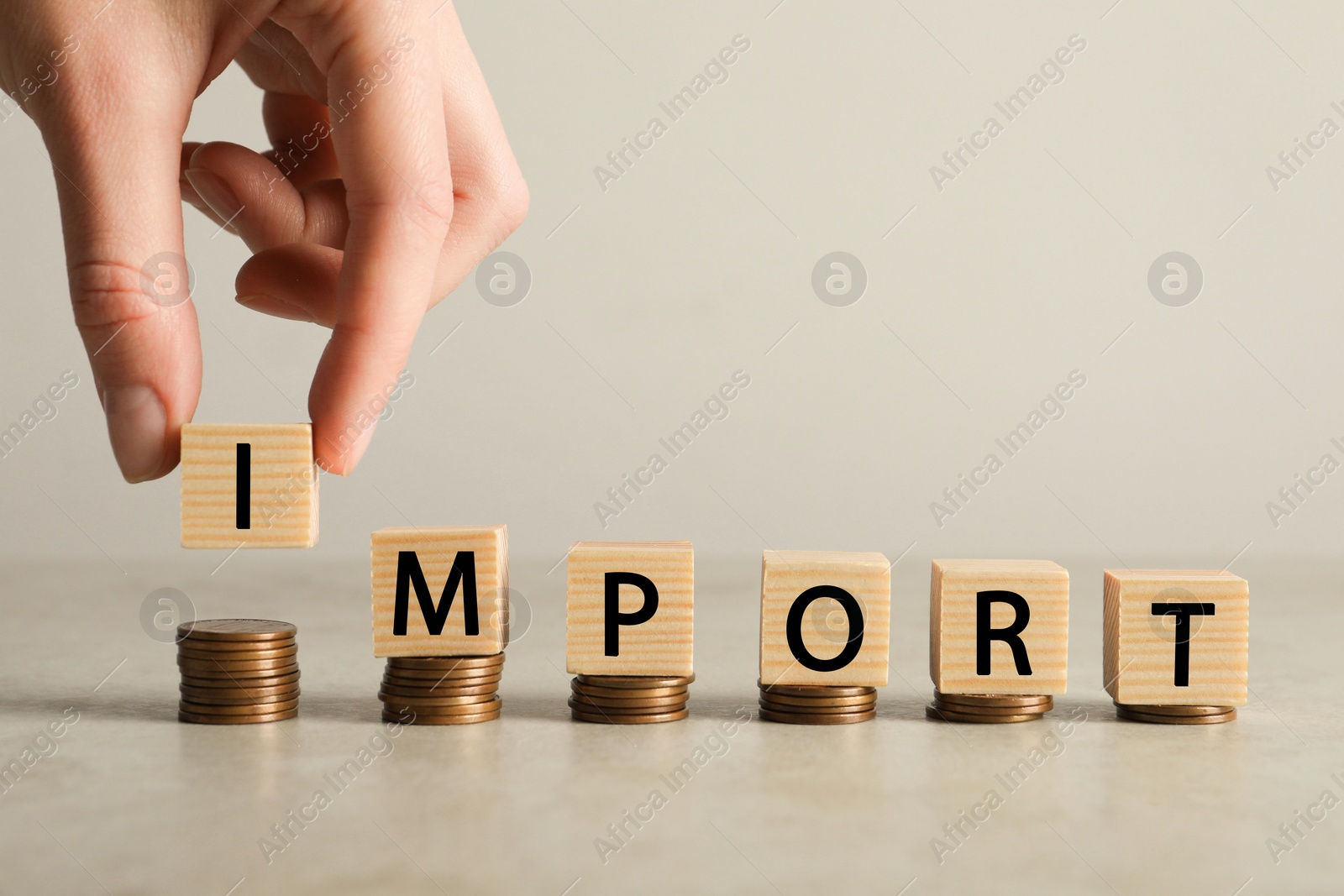 Photo of Woman putting cube with letter onto stacked coins to make word Import on light grey table, closeup