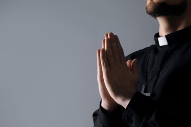 Photo of Priest praying on grey background, closeup. Space for text