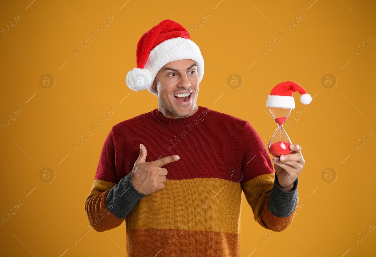 Photo of Man in Santa hat with hourglass on yellow background. Christmas countdown