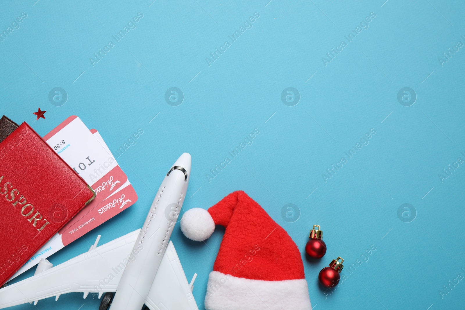 Photo of Santa hat, toy airplane, passports with airline tickets and space for text on blue background, flat lay. Christmas vacation