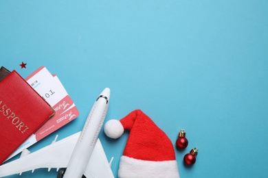 Photo of Santa hat, toy airplane, passports with airline tickets and space for text on blue background, flat lay. Christmas vacation