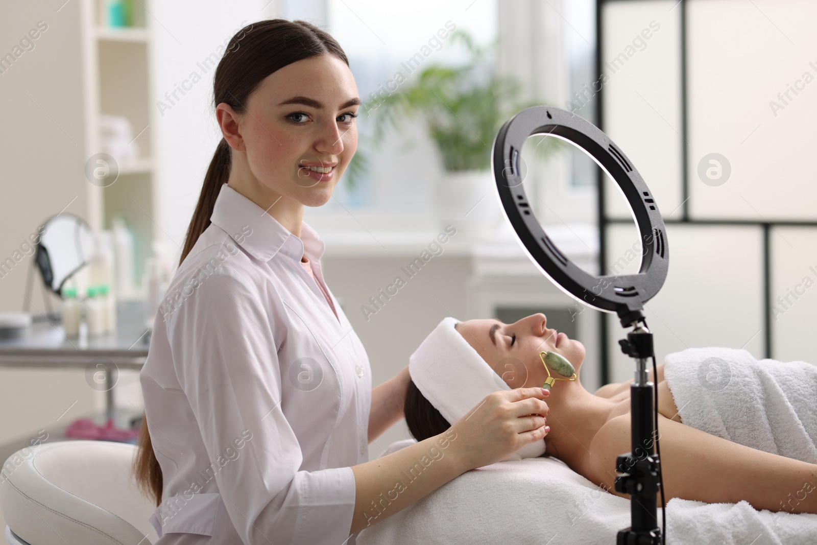 Photo of Cosmetologist making face massage with roller to client in clinic