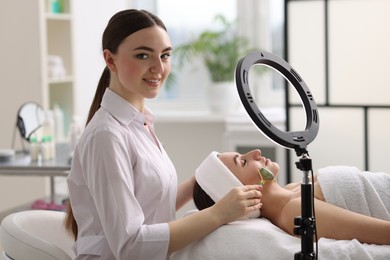 Photo of Cosmetologist making face massage with roller to client in clinic