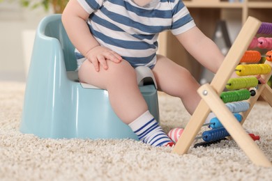 Photo of Little child sitting on plastic baby potty indoors, closeup