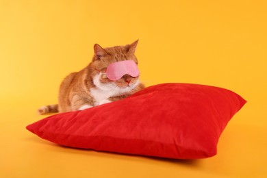 Photo of Cute ginger cat with sleep mask and red pillow on orange background