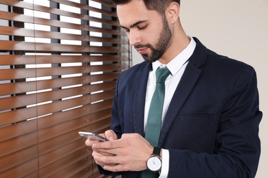 Photo of Portrait of businessman with mobile phone at window indoors, closeup. Space for text