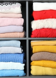 Photo of Many knitted winter clothes stacked on shelves on white background