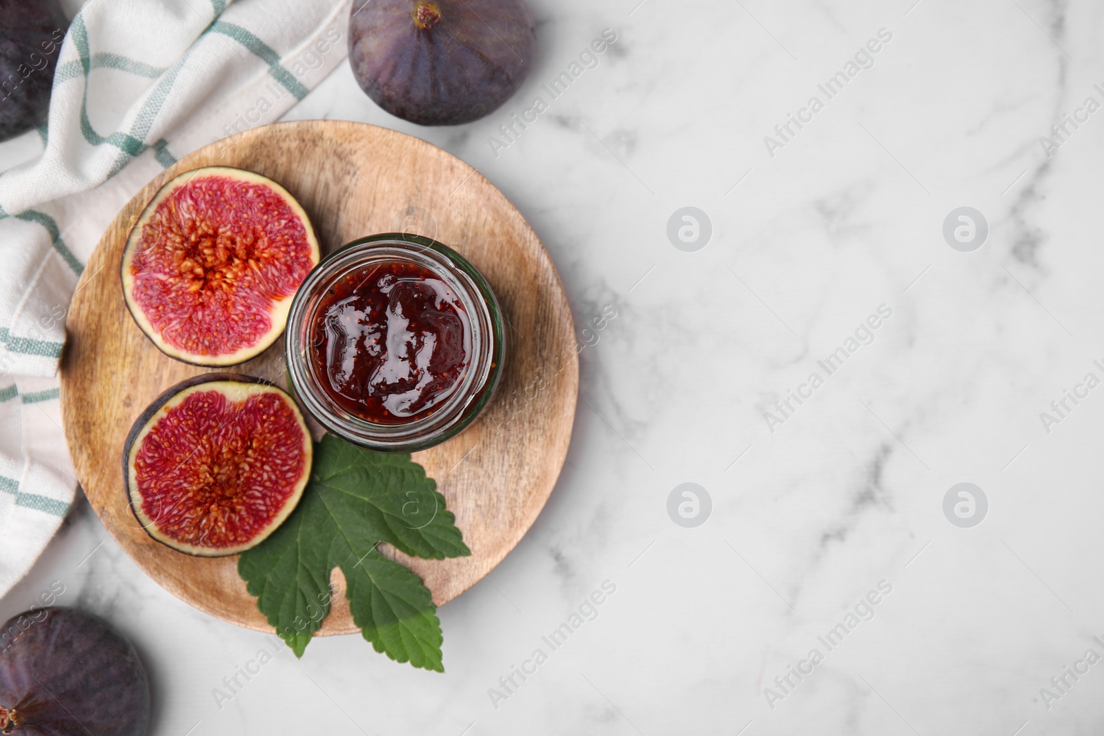 Photo of Glass jar of tasty sweet fig jam and fruits on white marble table, flat lay. Space for text