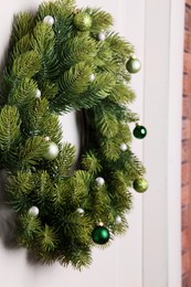 Photo of Beautiful Christmas wreath with festive decor hanging on white door, closeup