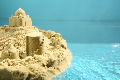 Pile of sand with beautiful castle on rippled water against light blue background, closeup. Space for text