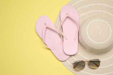 Photo of Flip flops, hat and sunglasses on yellow background, flat lay with space for text. Beach objects